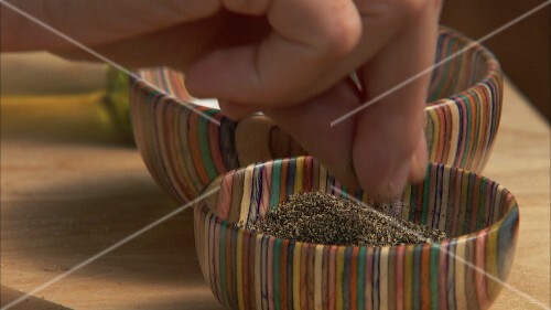 Hand taking salt and pepper out of colourful dishes