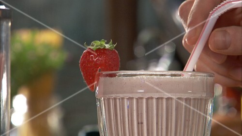 Pouring strawberry shake into glass and garnishing with strawberry