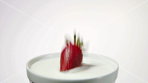 Eine Erdbeere fällt in Milch