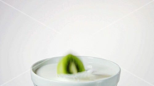 A slice of kiwi fruit falling into milk