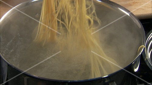 Putting salt and spaghetti into boiling water