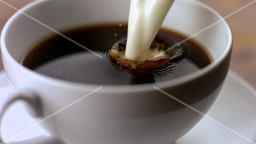 Putting milk into a cup of coffee