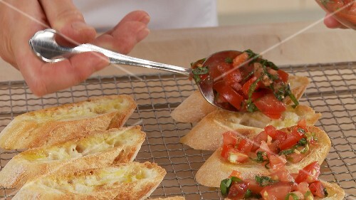 Preparing bruschetta: spreading the prepared tomatoes on the slices of bread