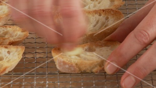 Garlic being rubbed onto slices of toasted bread