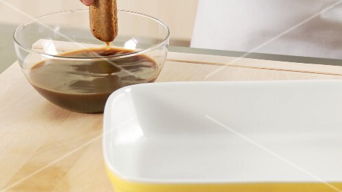 Preparing tiramisu: dunking a sponge finger in espresso and placing in a dish