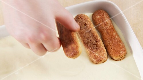 Preparing tiramisu: adding another layer of espresso biscuits