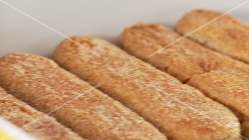 Tiramisu being prepared: espresso-soaked sponge fingers being placed in a dish