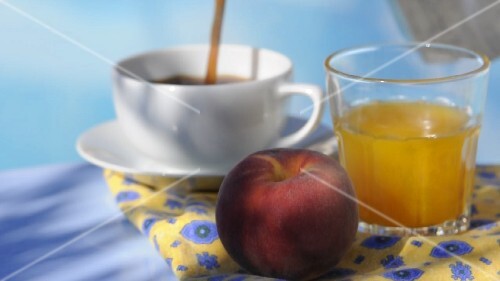 A breakfast tray at the pool: fruit juice, a peach and coffee being poured