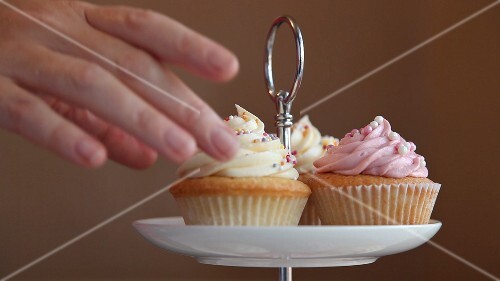 A hand taking a cupcake from a cake stand