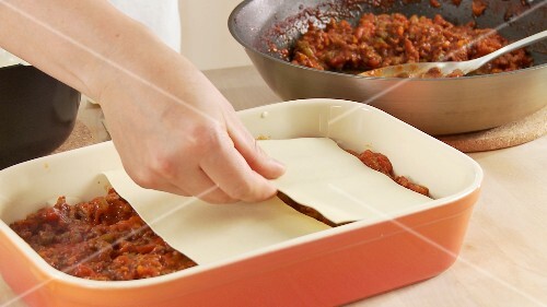 Minced meat sauce and lasagne sheets being layered in a baking dish