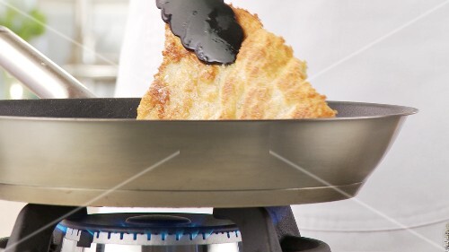 A breaded escalope being fried crispy in a pan