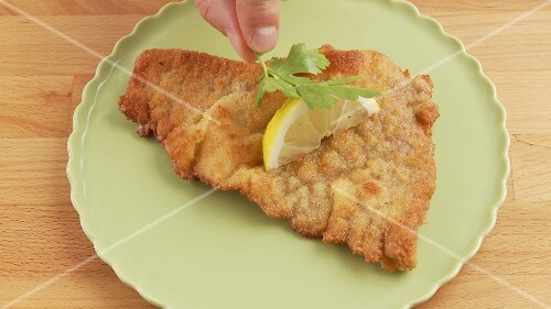 Escalope á la viennoise being garnished with a slice of lemon and a sprig of parsley