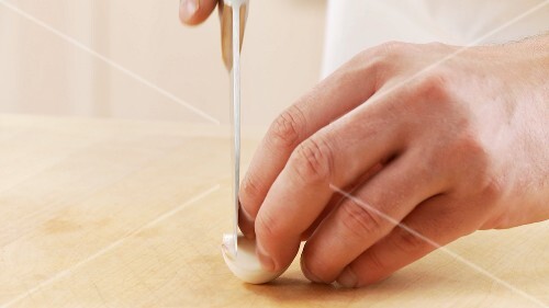 The lower end of a garlic clove being cut off
