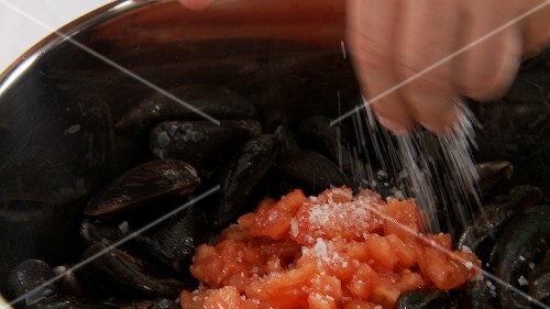 Tomato pieces being added to mussels and salted