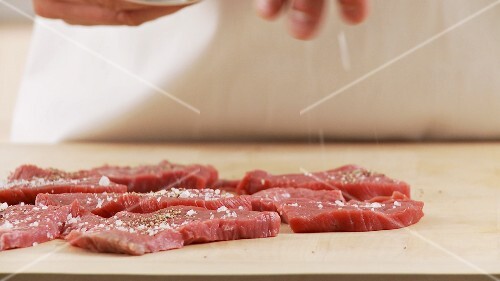 Veal escalopes being seasoned with salt