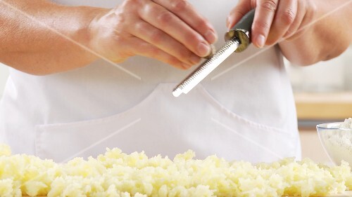 Cooked potatoes being seasoned with fresh, grated nutmeg