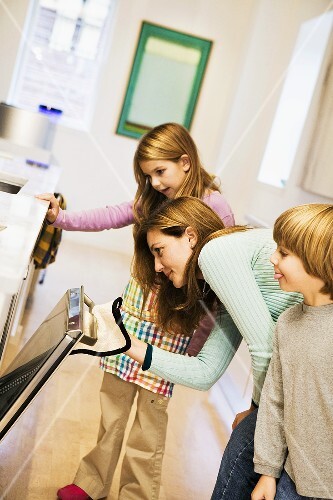 A Woman Opening the Oven Door with Two Children