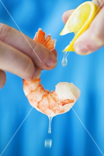 Hand Squeezing Lemon Onto a Shrimp