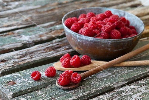 Raspberries in a metal bowl and on a wooden spoon on rustic wooden boards