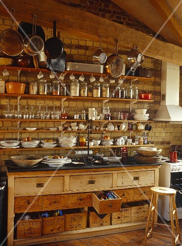 Resting against the end brick wall of the kitchen is a dresser with a slate top and wooden drawers made from old wine boxes as well as shelves crammed with kitchen utensils