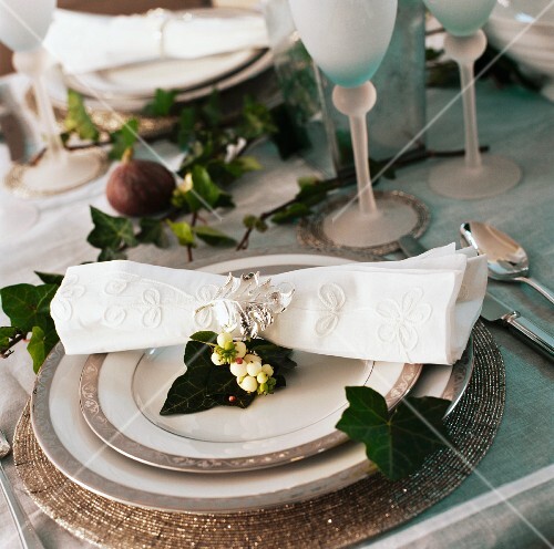 Close-up of cream linen napkin on pewter-edged plates on Christmas table decorated with ivy leaves