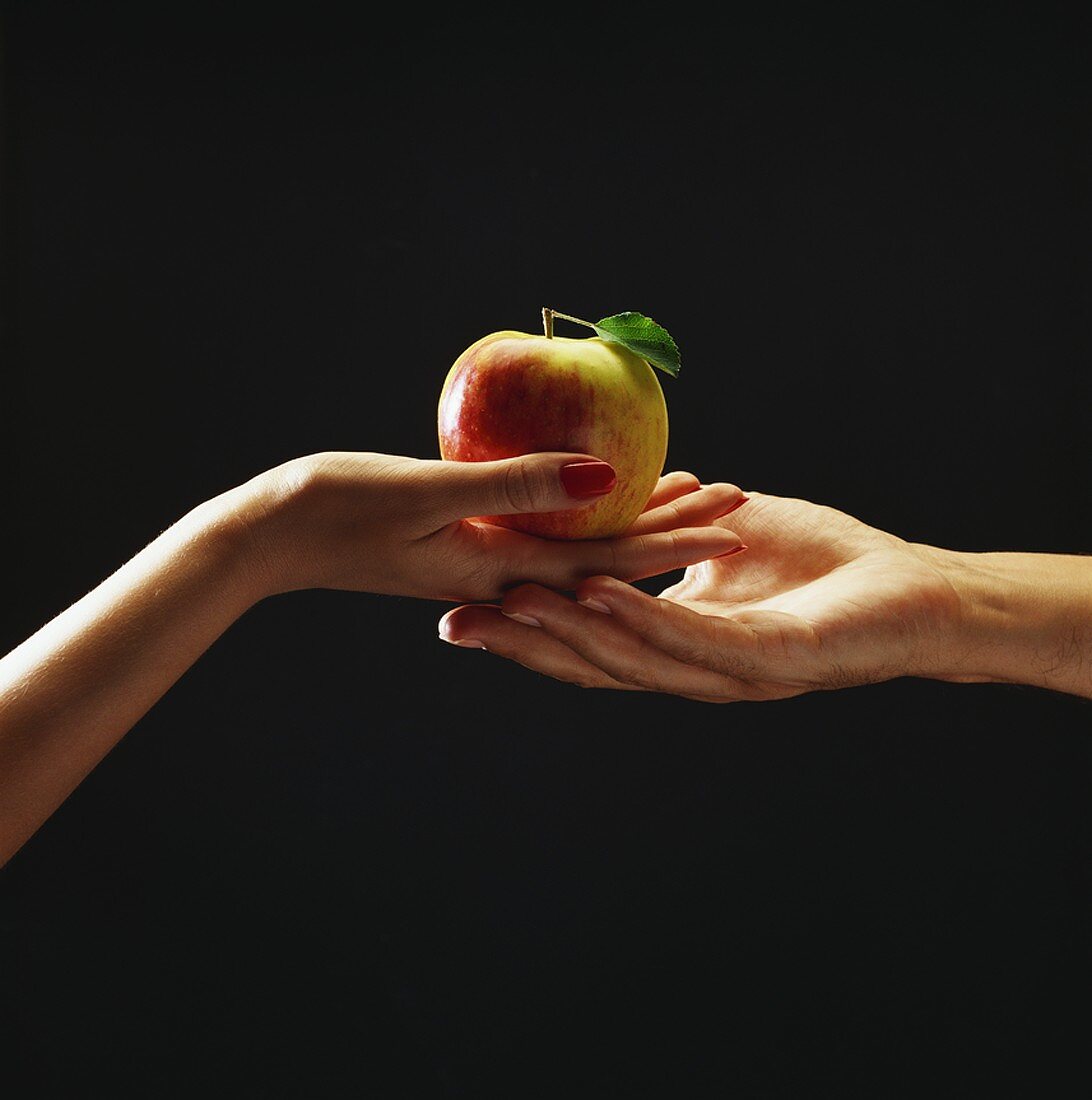 Woman's hand passing apple to man's hand