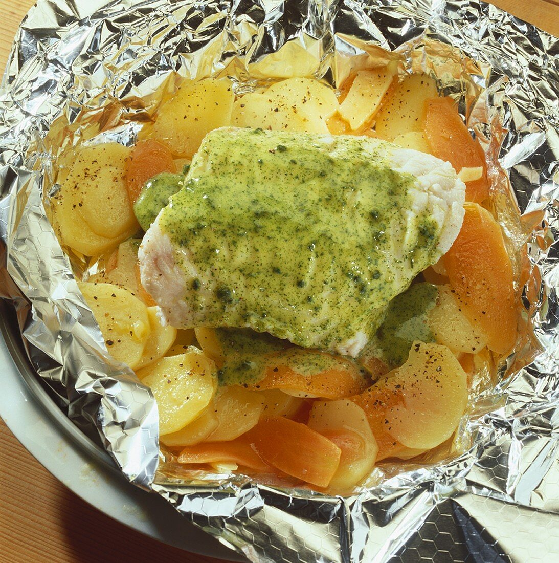 Fish fillet in foil with potatoes, carrots and herb sauce