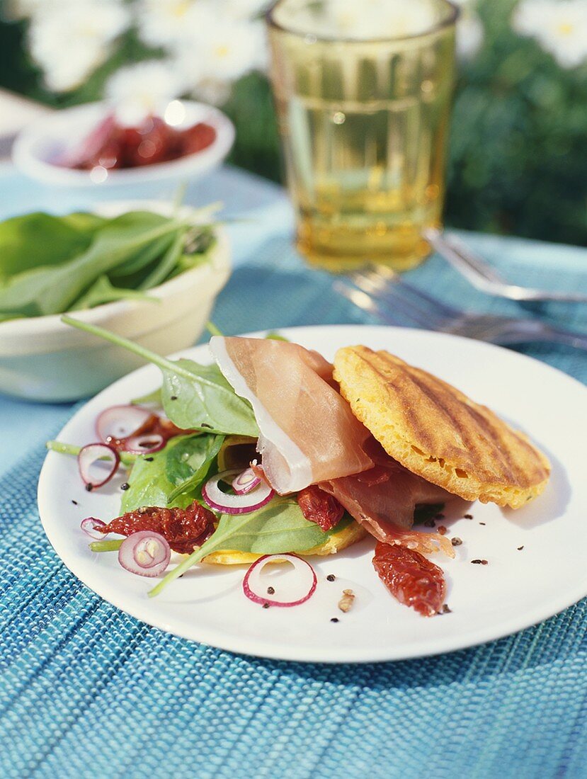 Grilled corn cakes with prosciutto and Mediterranean salad
