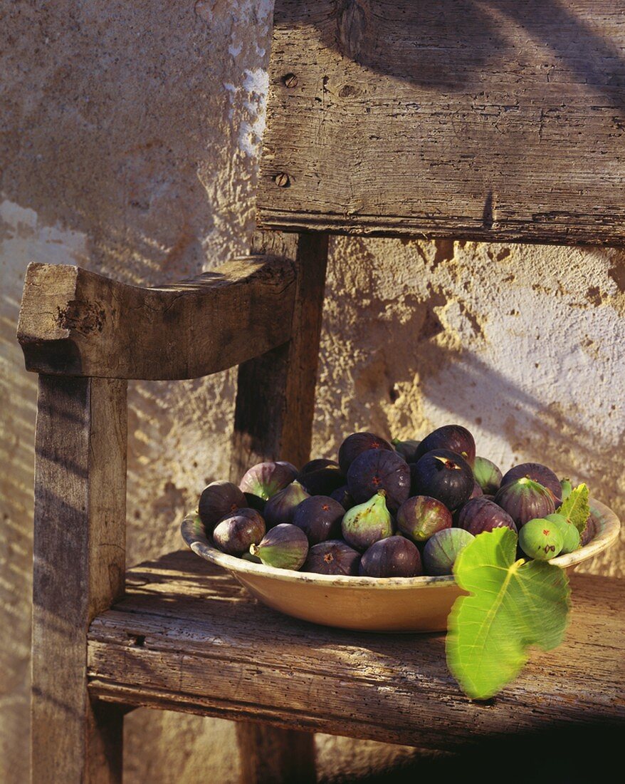Figs in earthenware dish on wooden bench out of doors