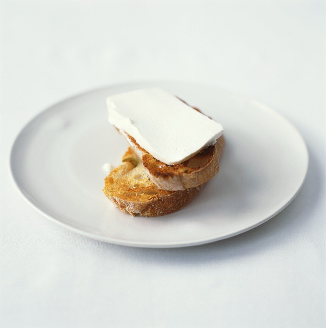 Toasted baguette slices with ricotta on white plate