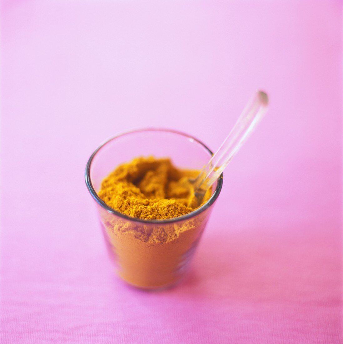 Ground turmeric in a glass, pink background