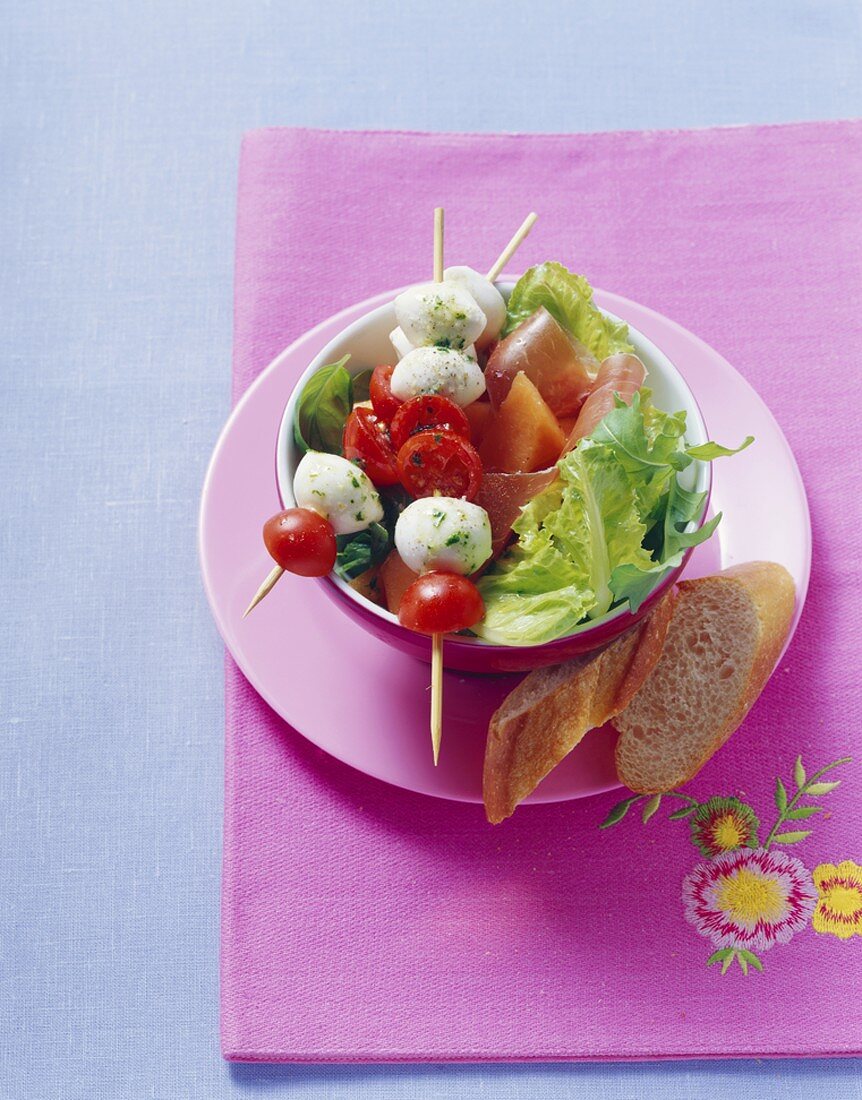 Tomaten-Mozzarella-Spieße auf grünem Salat, Schinken, Melone