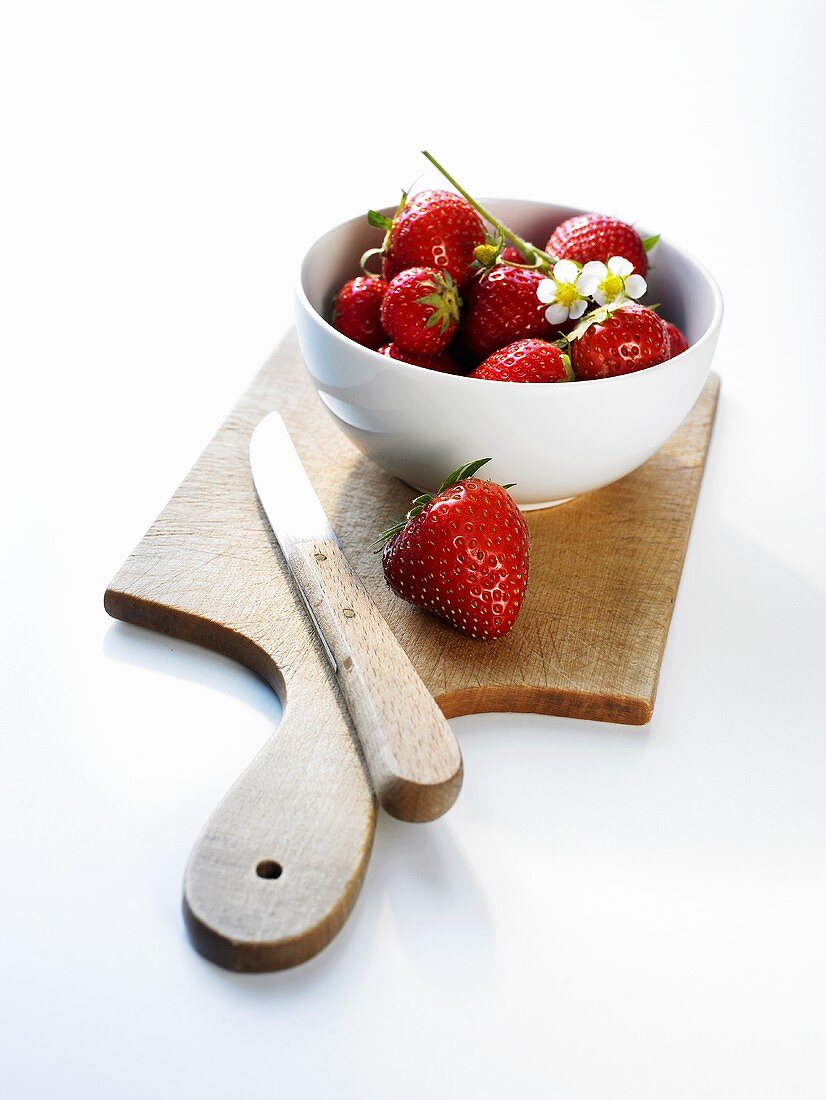 Several strawberries in a small bowl on a wooden board
