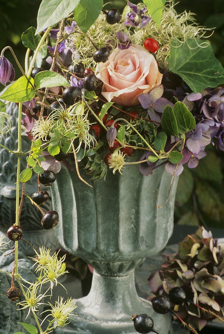 Gesteck mit schwarzen Hagebutten, Clematis und einer Rose