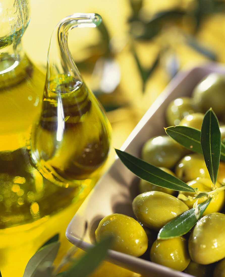 Grüne Oliven und eine Karaffe mit Olivenöl
