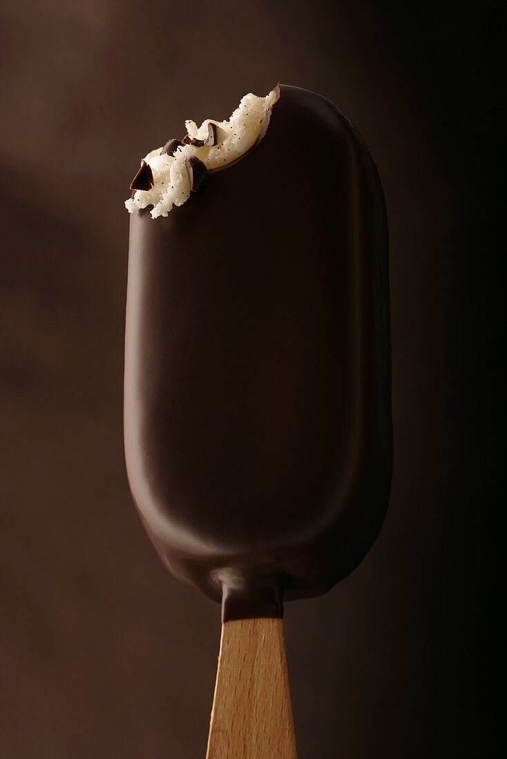 A chocolate-covered ice cream on a stick, with a bite taken