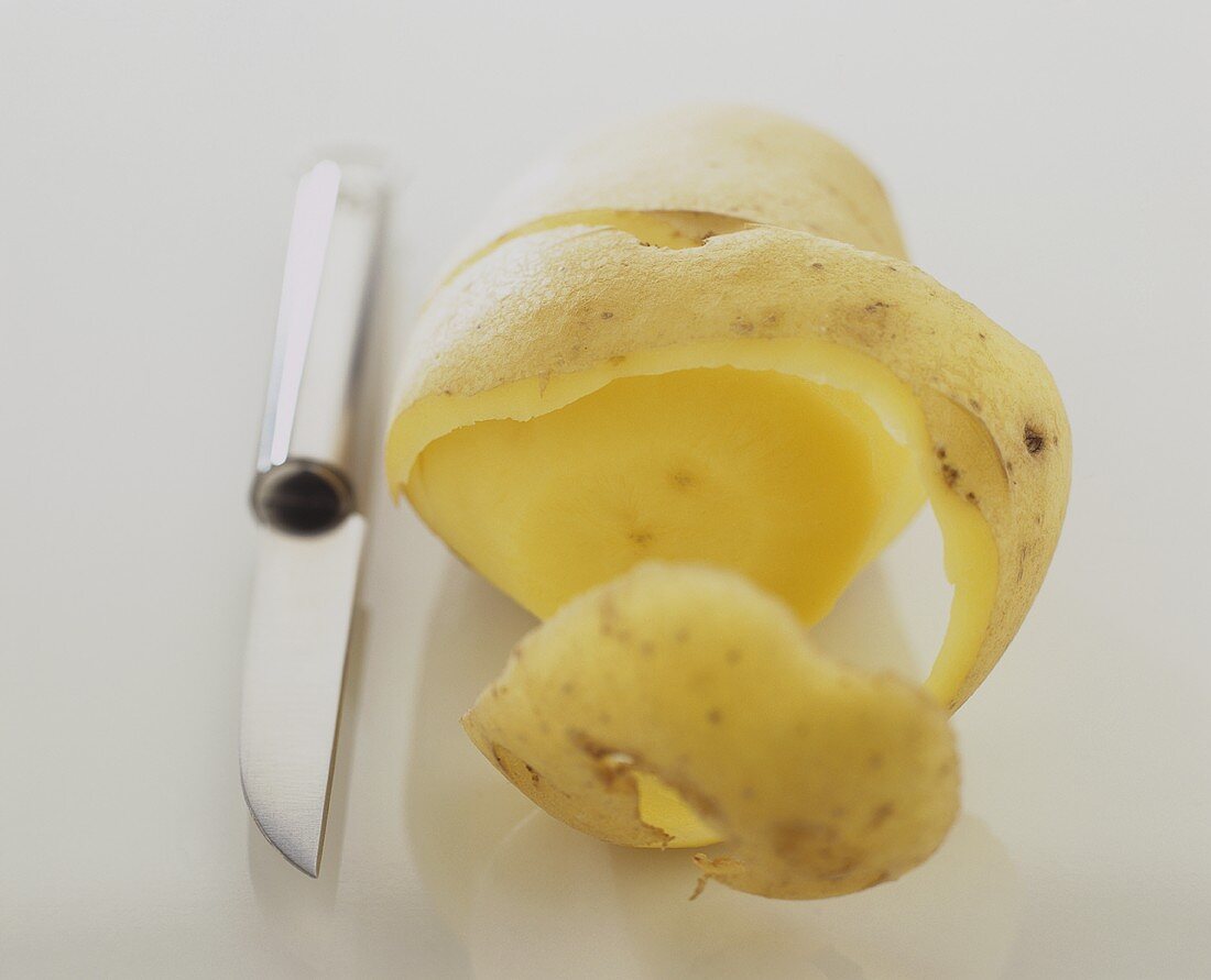 Peeled potato with peel and a kitchen knife