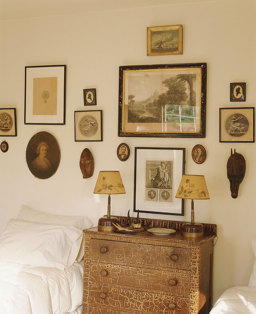 Antique chest of drawers between twin beds below collection of antique pictures