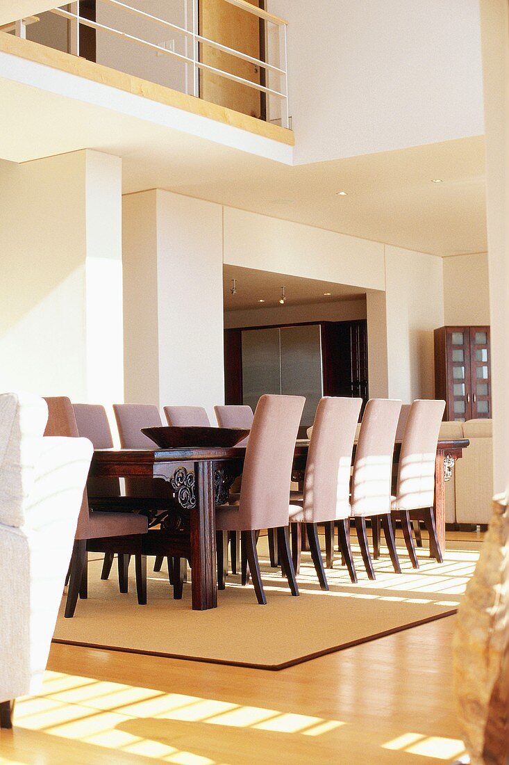 Dining area in open-plan interior with long dining table, upholstered chairs and gallery