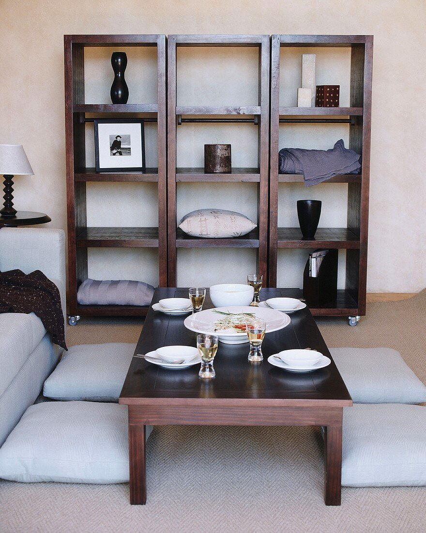 Square wooden shelving units on castors and coffee table set for four people surrounded by floor cushions