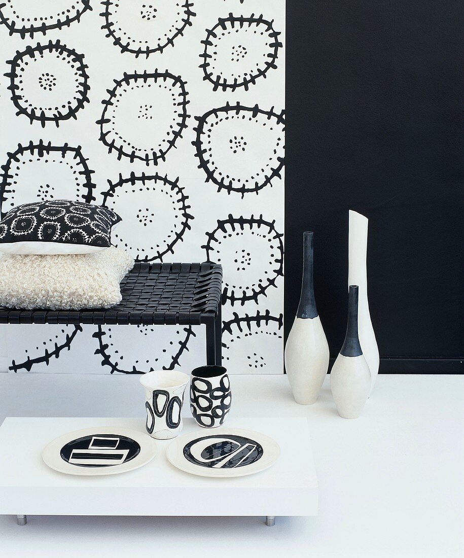 Still-life arrangement in black and white with bench, floor vases and patterned wallpaper