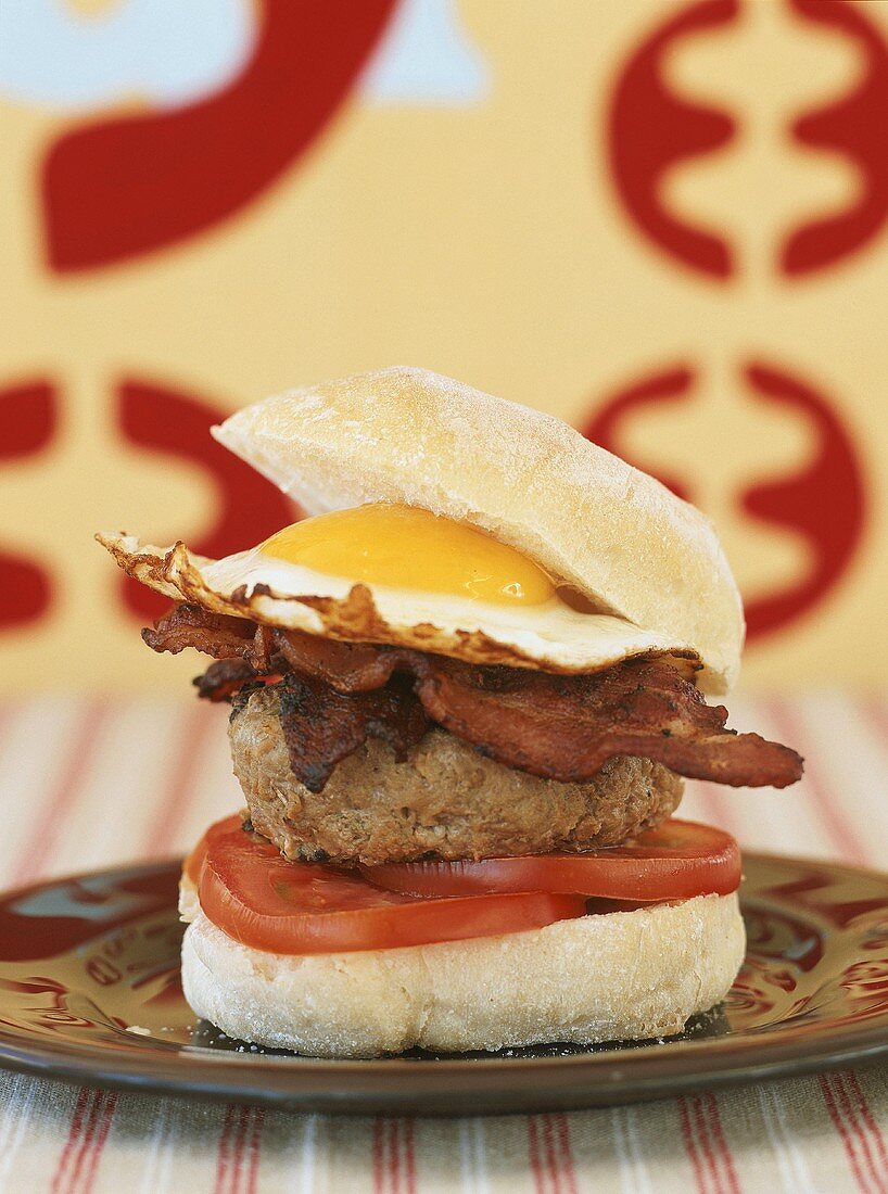 A hamburger with tomato, bacon and fried egg