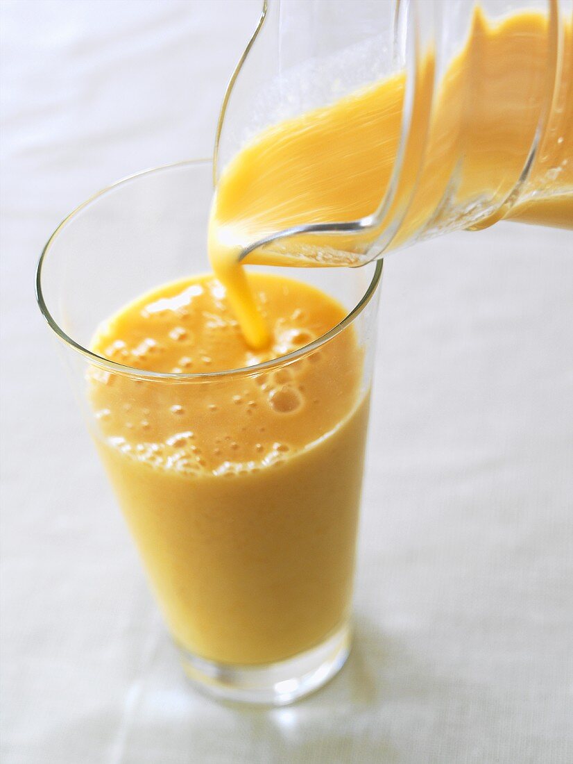 Orangen-Joghurt-Drink von der Kanne ins Glas eingießen