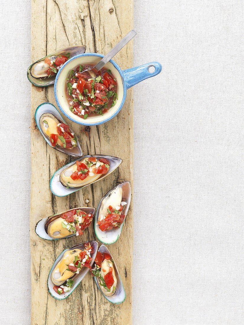 Steamed mussels with salsa topping on a plank of wood