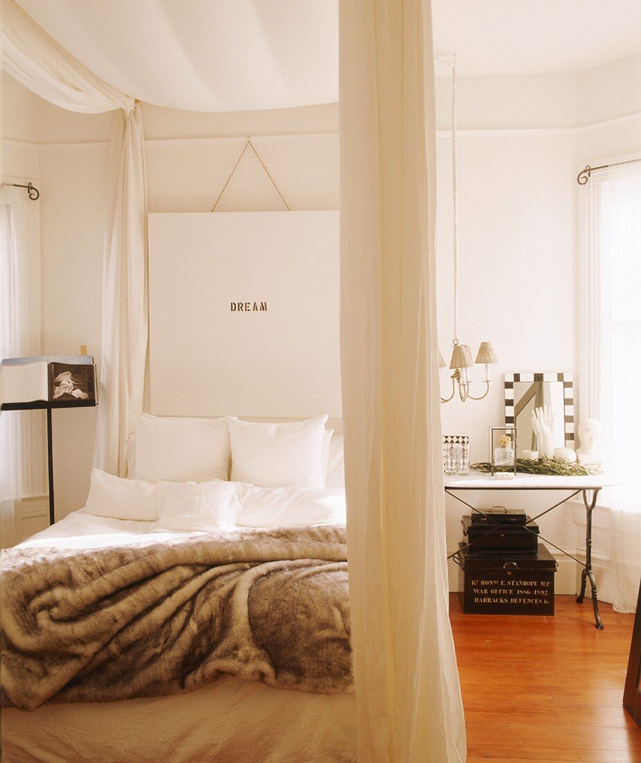 Four-poster bed with white curtains and soft fur blanket; white artwork with lettering above head of bed