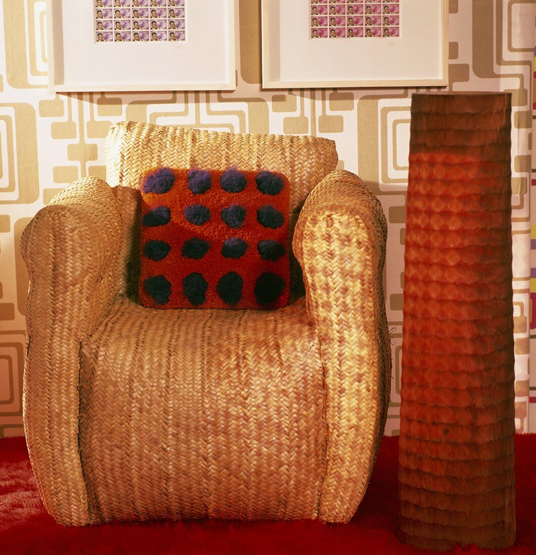 Aussergewöhnlicher Korbsessel mit Filzkissen und orangefarbener Stehlampe daneben; dahinter eine Wandtapete im Stil der 70iger Jahre