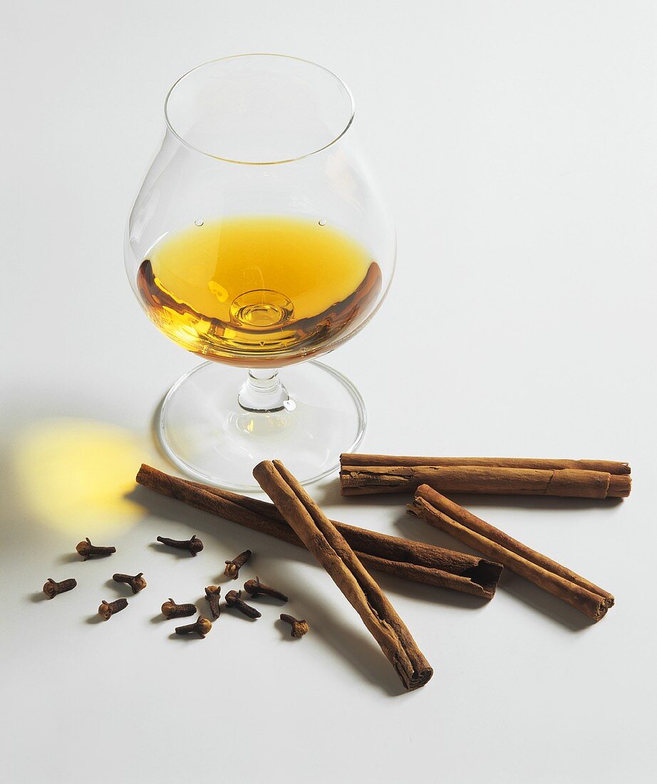 A glass of cognac with cinnamon sticks and cloves