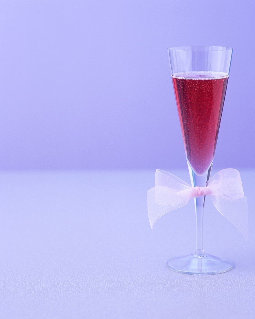 Ein Glas roter Sekt-Cocktail mit Schleife am Glas