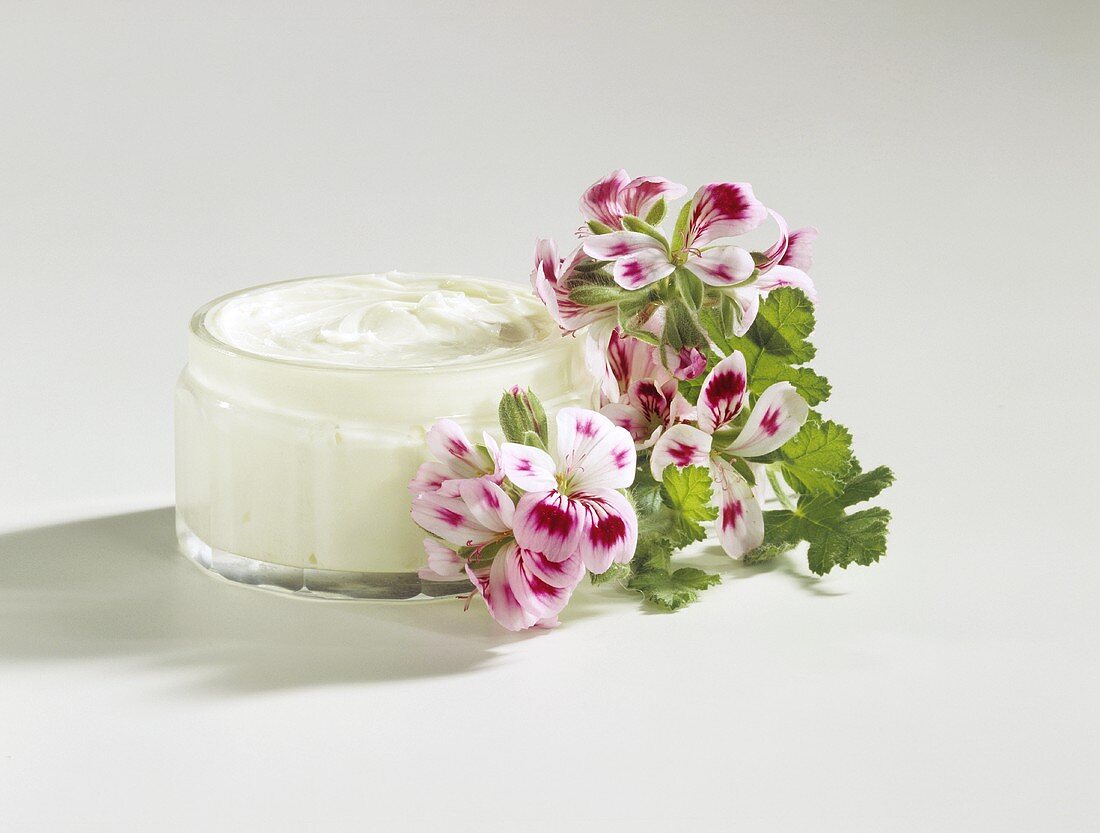 Home-made skin cream in glass jar, flowers beside it