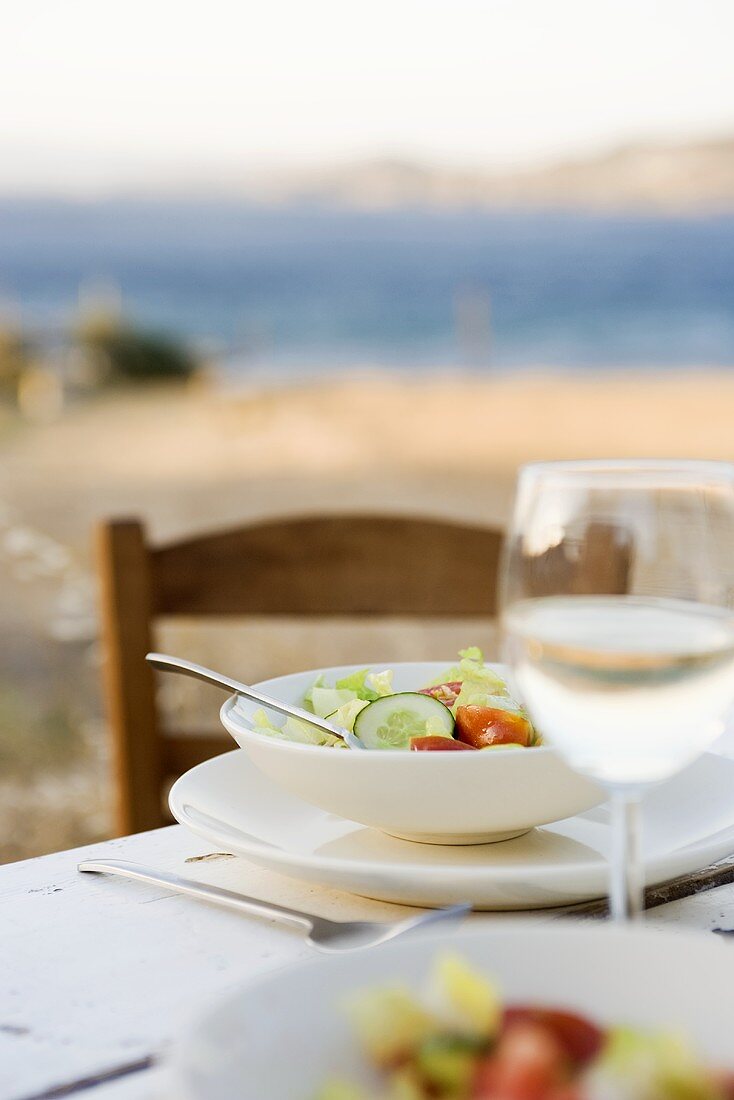 Salad and white wine on laid table by the sea